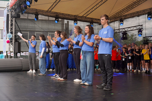 Mehrere Personen mit blauen T-Shirts tanzen auf der Bühne.