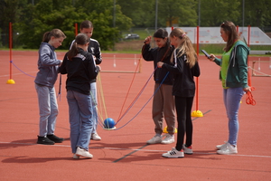 Kinder tragen gemeinsam einen Tennisring an Seilen.