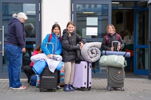 Kinder stehen mit ihren Koffern vor einer Schule.