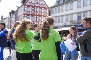 Zwei Frauen in grünen T-Shirts hören einer anderen jungen Frau zu.