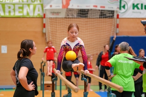 Ein Kind turnt an einem Parallelbarren mit einem Ball. 