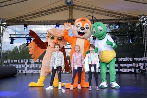 Die drei Maskottchen der Hessischen Turnjugend posieren mit Kindern auf der Bühne.