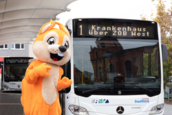 Das Maskottchen Freddy steht an einem Busbahnhof.