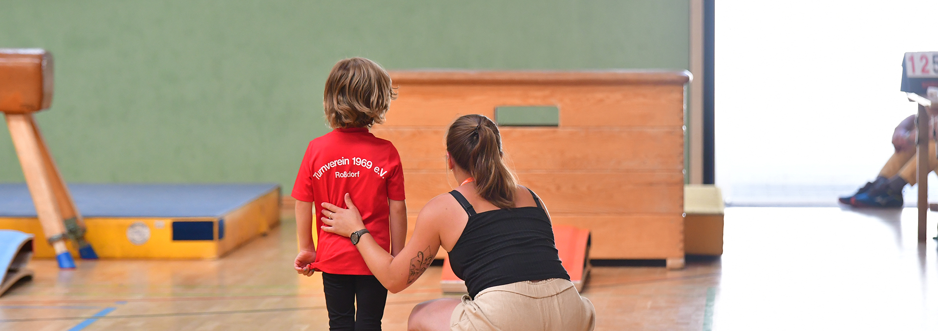Eine Frau unterstützt einen kleinen Jungen bei seiner Turnübung.