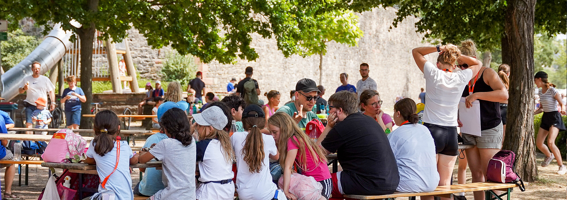 Familien mit Kindern sitzen draußen auf einer Bank auf der Turnfestmeile.