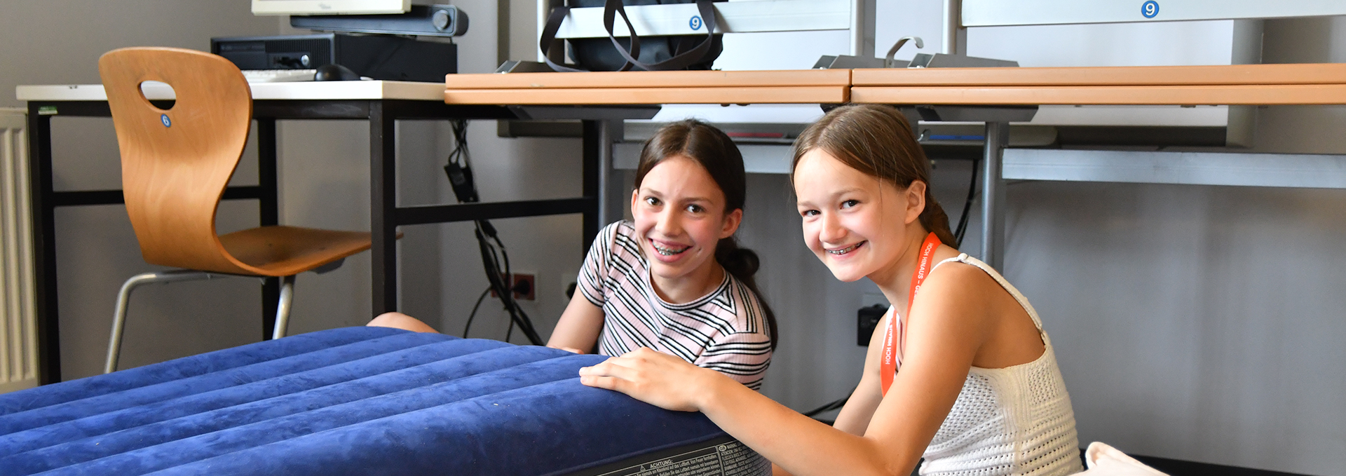 Zwei Mädchen blasen eine Luftmatratze auf.