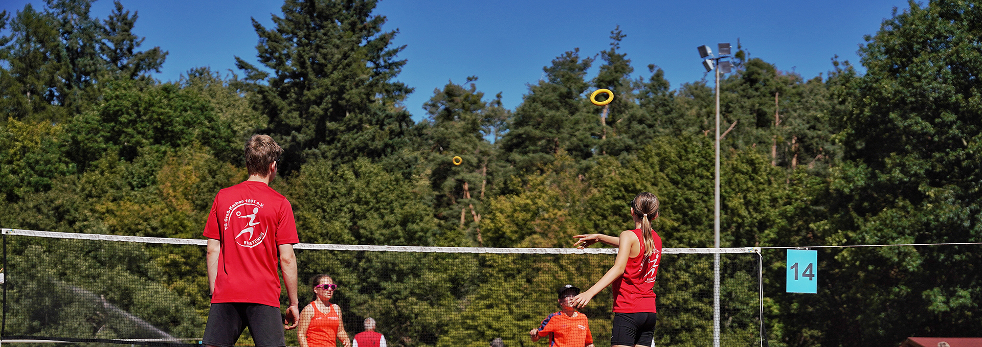 Mehrere Sportler und Sportlerinnen spielen Ringtennis auf einem Outdoor-Feld.